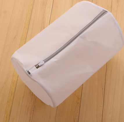 A white cylindrical zippered storage bag or sleeve with a gray zipper, shown on a light wood plank floor.