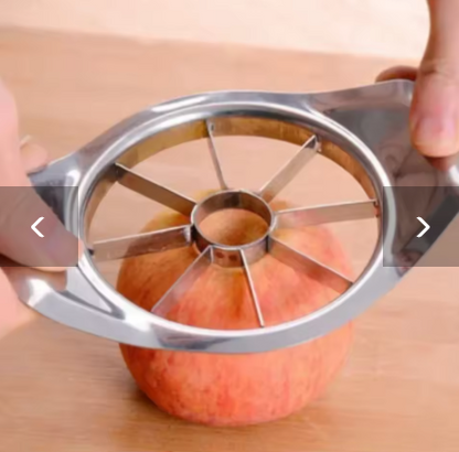 A stainless steel apple corer and slicer being used on an apple on a wooden surface, with hands holding the handles.