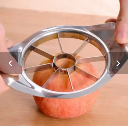 A stainless steel apple corer and slicer being used on an apple on a wooden surface, with hands holding the handles.