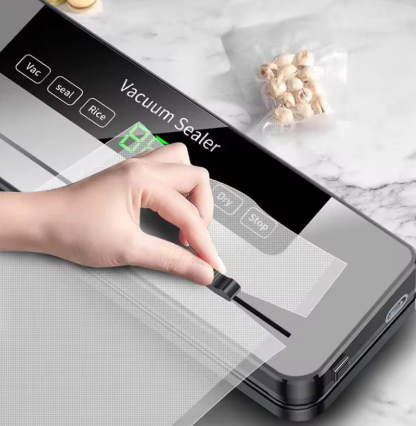 A close-up of a hand using a clear adhesive strip to seal a small vacuum-sealed pouch on a countertop. The device screen reads 'Vacuum Sealer' with settings like Vac, seal, and Rice, and a small bag of nuts sits nearby on a light marble surface.