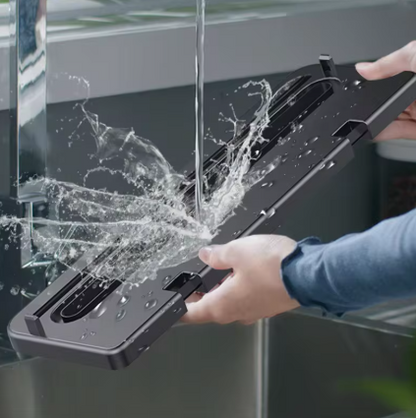 A person holds a black rectangular glass-cleaning tool or panel in front of a glass surface, with water sprayed onto it. The product is shown in use in a real environment, so this is Lifestyle rather than Product/Packaging.