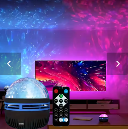 A small portable projector lamp with a clear dome and black base sits on a table in a living room setup, alongside a remote control. The room is lit with colorful projected light showing blue, purple, and pink abstract patterns on the wall and above a TV.