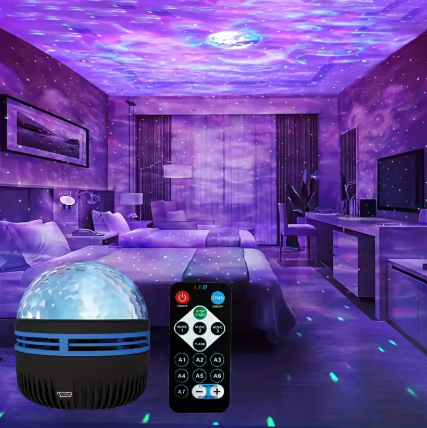 A purple galaxy night light projector shown in a bedroom setting, with the product and its remote control overlaid in the foreground. The room is illuminated with a starry sky pattern on the ceiling and floor.