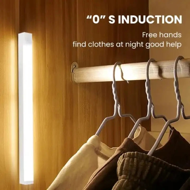 A vertical LED light strip mounted on a wooden closet door, illuminating a clothing rack with hangers and garments. Text on the image reads '0" S INDUCTION' and 'Free hands find clothes at night good help.