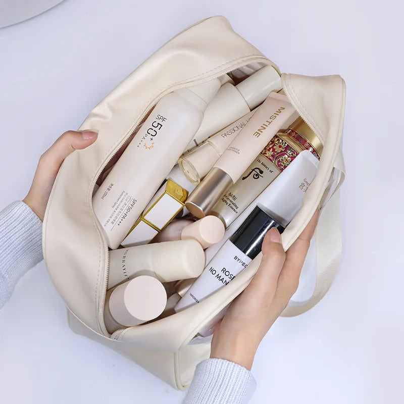 Beige cosmetic bag filled with skincare products held by a person against a white background