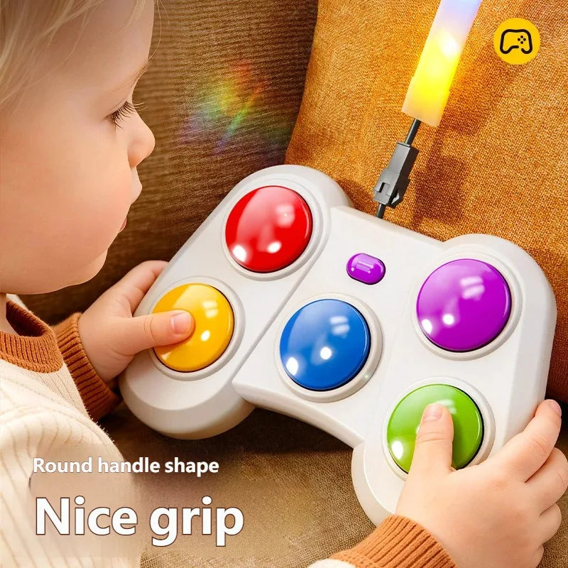 A child holds a white toy game controller with colorful round buttons while sitting on a brown couch. The controller has red, yellow, blue, purple, and green buttons, and a small light bar attached at the top glows yellow.