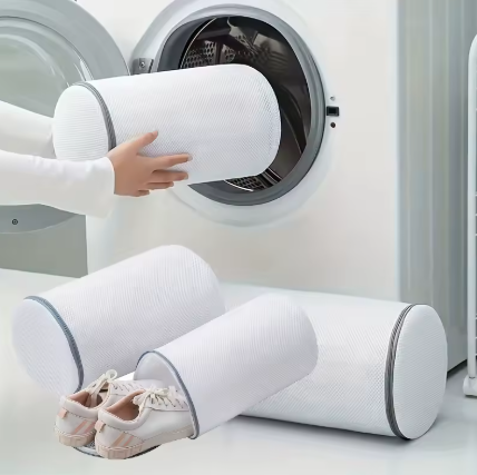 White cylindrical sock cover sleeves with gray trim being demonstrated in a laundry setting, with one sleeve being inserted into a washing machine and a pair of socks inside a sleeve on the floor.