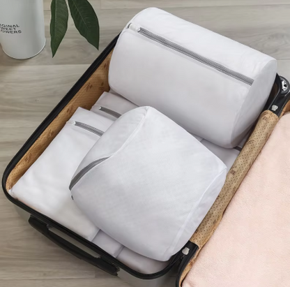 Three white packing cubes with silver zippers neatly arranged inside an open suitcase on a light wood floor.
