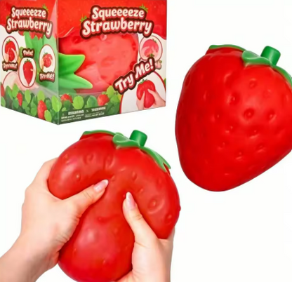 A red strawberry-shaped squishy toy shown with a person's hands squeezing it, plus the retail box labeled 'Squeezeze Strawberry' on a white background.