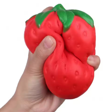 A hand holding a red strawberry-shaped squishy toy against a plain white background.